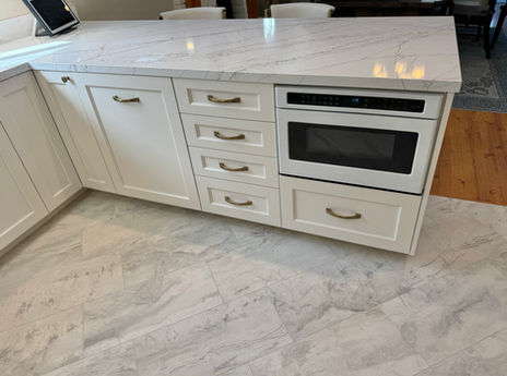 White kitchen island with built-in microwave and drawers, marble countertop, hardwood floors.