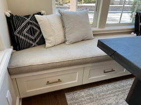 Cozy window seat with pillows and storage drawers, provides relaxing comfort.