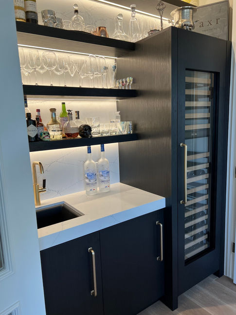 Modern home bar with glasses, bottles, and a sleek wine fridge.