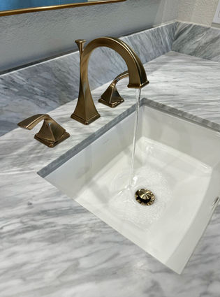 Elegant golden faucet with flowing water in a white bathroom sink built-in to a marble countertop.