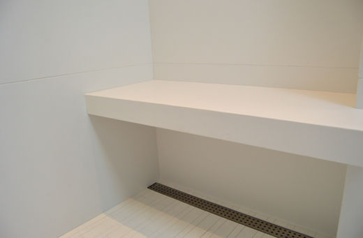 Large white shower bench/shelf with a water drain for shampoo and soap.