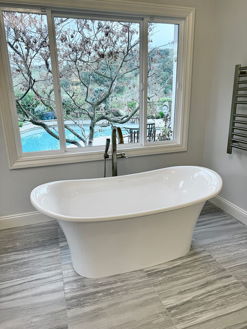White bathtub by the window overlooking a serene pool area.