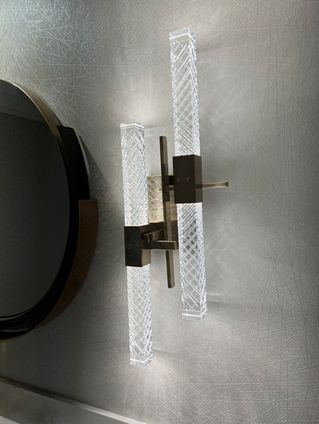 Modern wall sconce with bright tube lights, next to a round mirror, on wall.