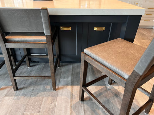 Two bar stools near a countertop with tan cushions and wooden frames.