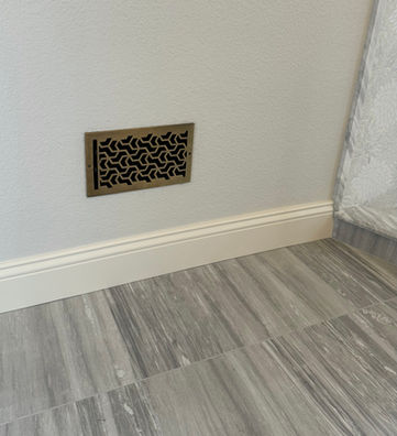 Decorative vent on white wall above baseboard and gray tiled floor