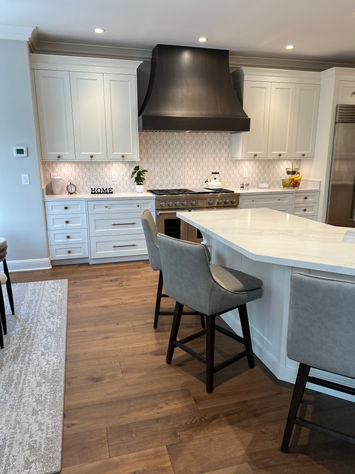 Modern white kitchen with island, cabinets, and dark hood range, ready to use.