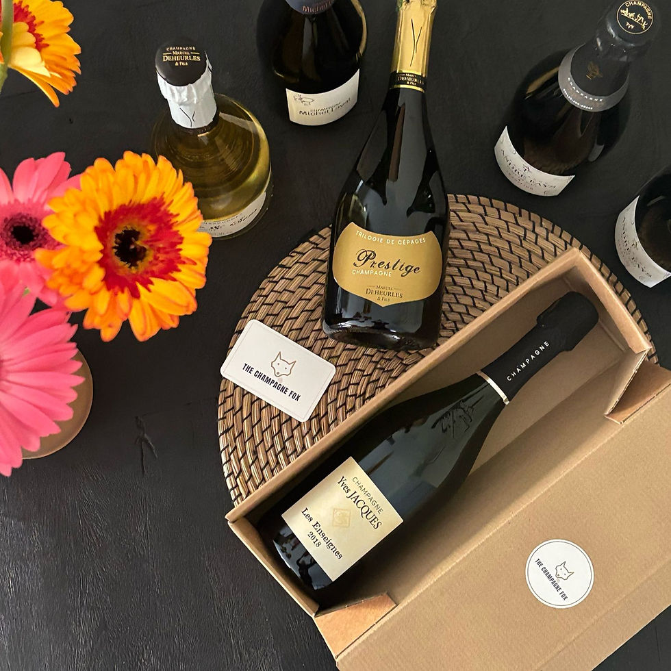 Champagneflessen op een donkere tafel met felgekleurde bloemen. 'The Champagne Fox'-tekst op kaarten en doos. Feestelijke sfeer. Een voorbeeld van ons maandelijkse wijnabonnement, The Champagne Box.