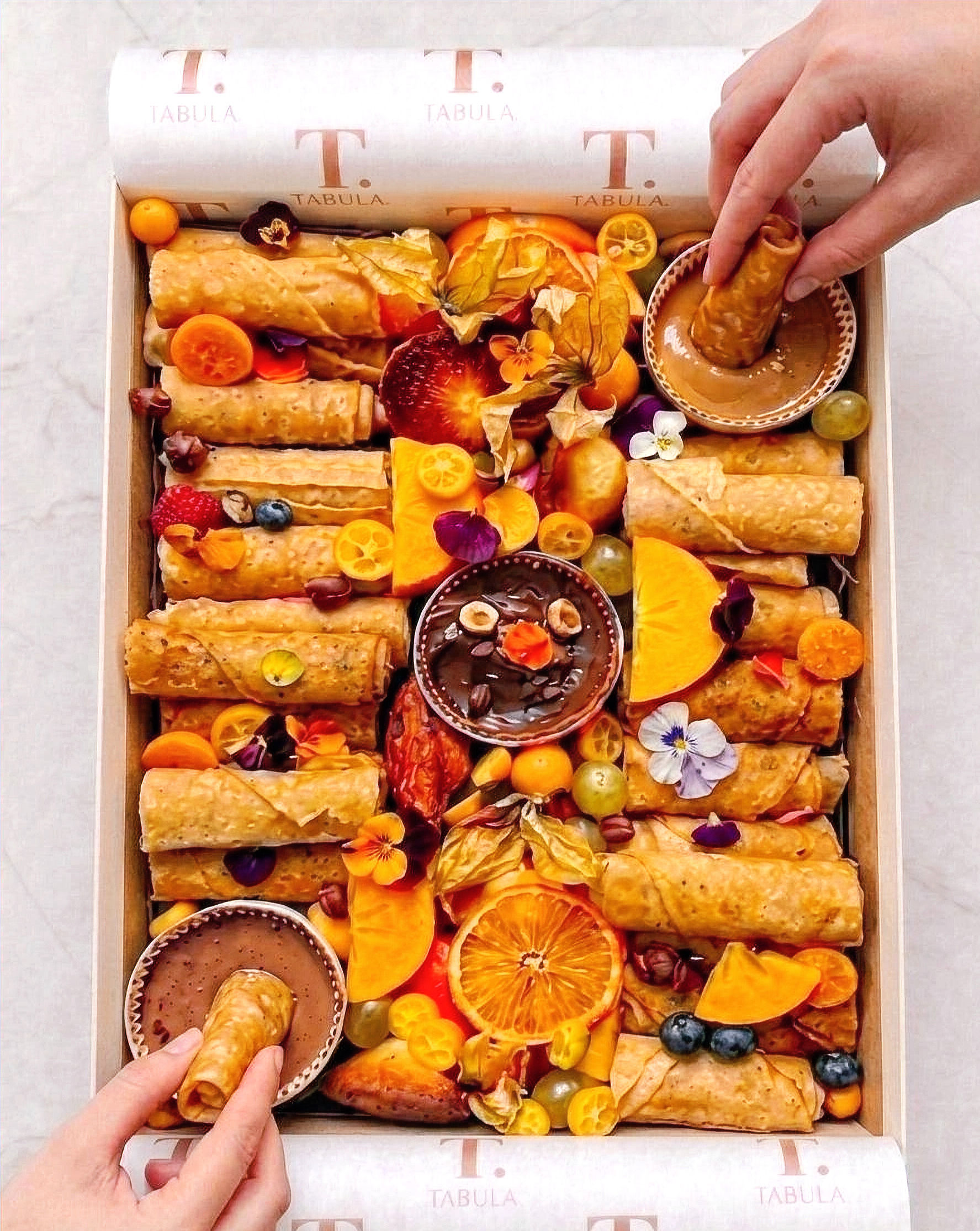 Rolled crêpes with chocolate and caramel dips, fresh fruit and edible blossoms