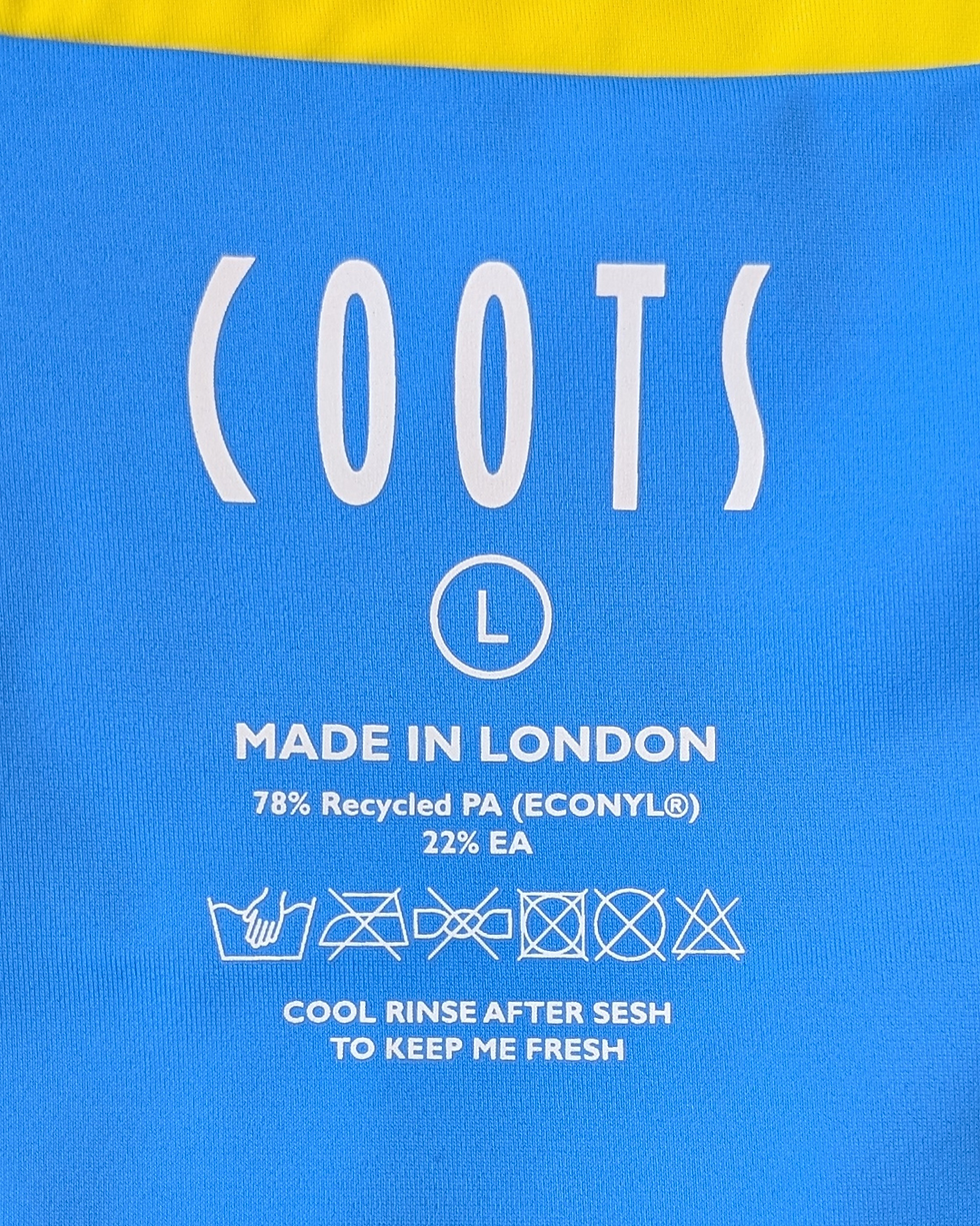 Blue garment label reads "COOTS," "L," "Made in London," with fabric content and care symbols. Yellow accent on top edge.