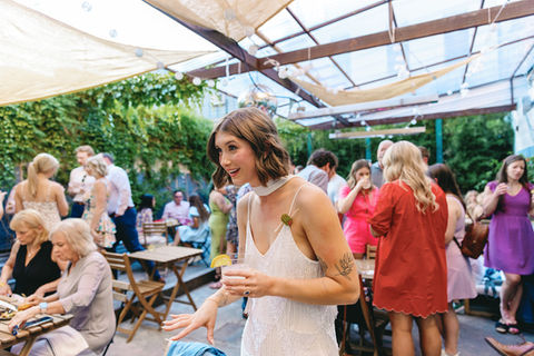 Future bride celebrating her engagement party under the covered backyard patio at BABA, surrounded by friends, family, natural wines, cocktails, and food platters in Williamsburg, Brooklyn.