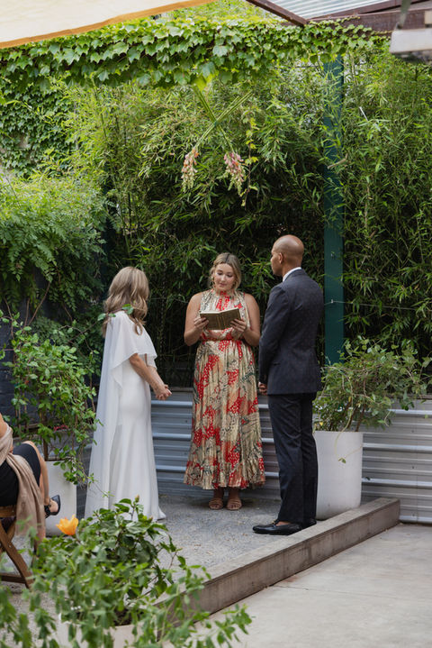 Intimate wedding ceremony at BABA Williamsburg’s backyard with a lush green backdrop and close friends gathered.