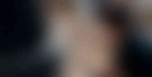 Man crouched, assembling white pipe on a large black barrel supported by tires; outdoor setting, casual mood, sunny day.