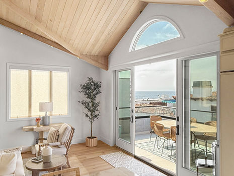 Bright, modern living room with vaulted wood ceiling, marble counter, and glass doors opening to a patio with ocean view; cozy and serene.