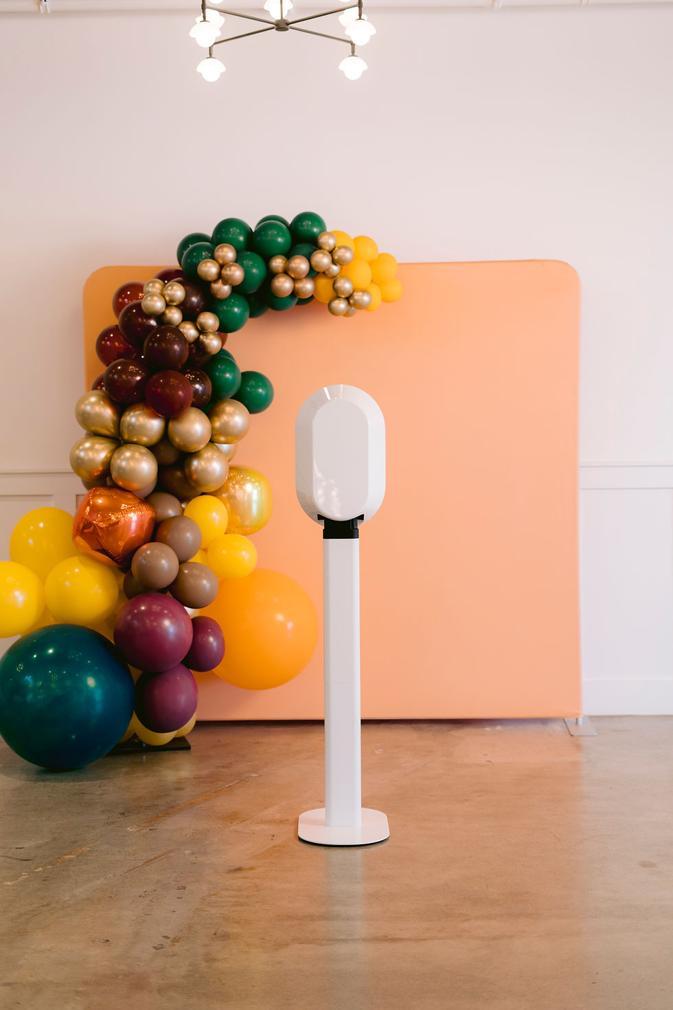 White photo booth in front of a peach backdrop with colorful balloon garland