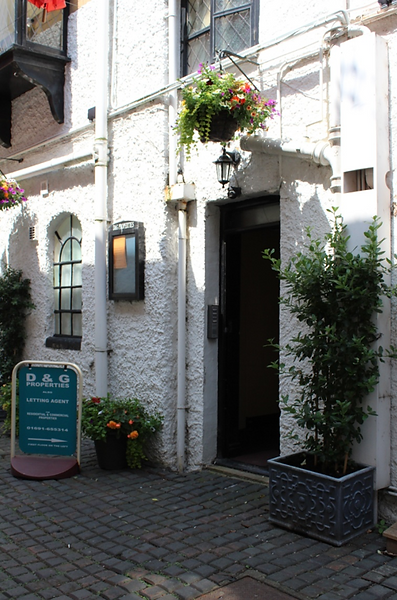 Alleyway with flower pots and hanging baskets of flowers with D&G Properties sign pointing to office