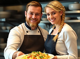 Handsome male chef  with a beard handing a pasta platter to an attractive blonde haired fe