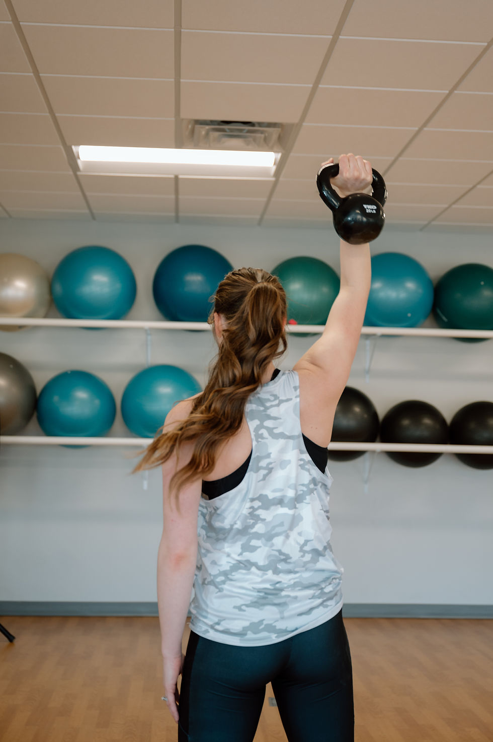 woman holding a kettle bell overhead in a gym 