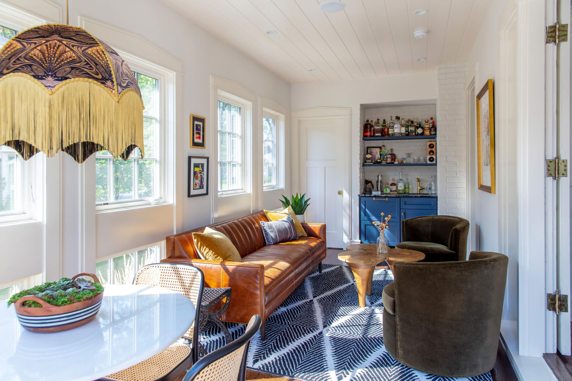 Sunroom design with Anna Hayman light fixture, leather sofa, and olive green velvet chair.