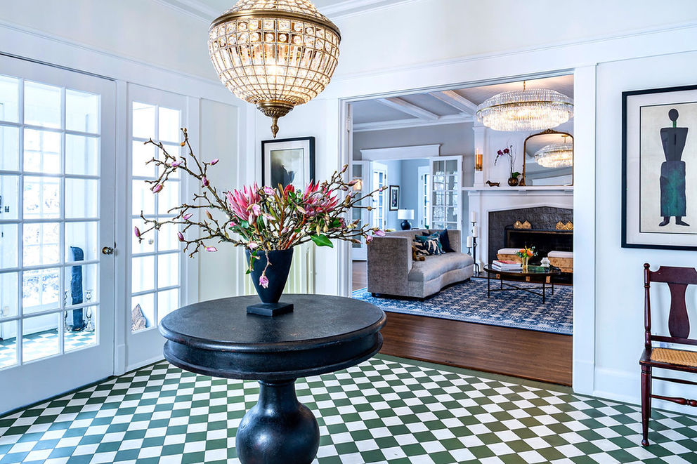 Checkered green and white floor in a foyer, elegant lighting, and black wooden round tables.
