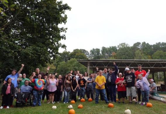 A large group stands outdoors with pumpkins in front of them during the community event.