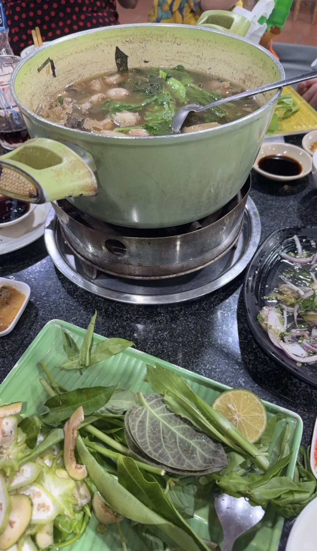 Goat hotpot on a burner, with a plate of fresh leaves and vegetables.