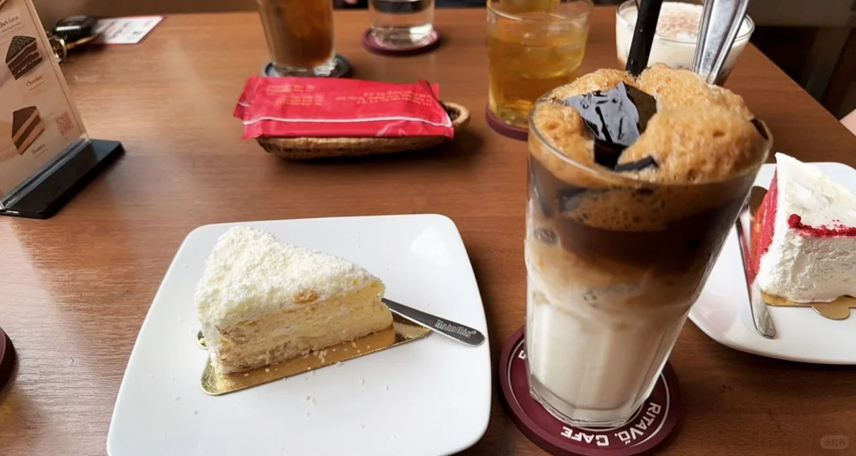 Iced coffee and a slice of pale corn cake on a café table.