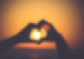 Hand making heart shape with sun in background.
