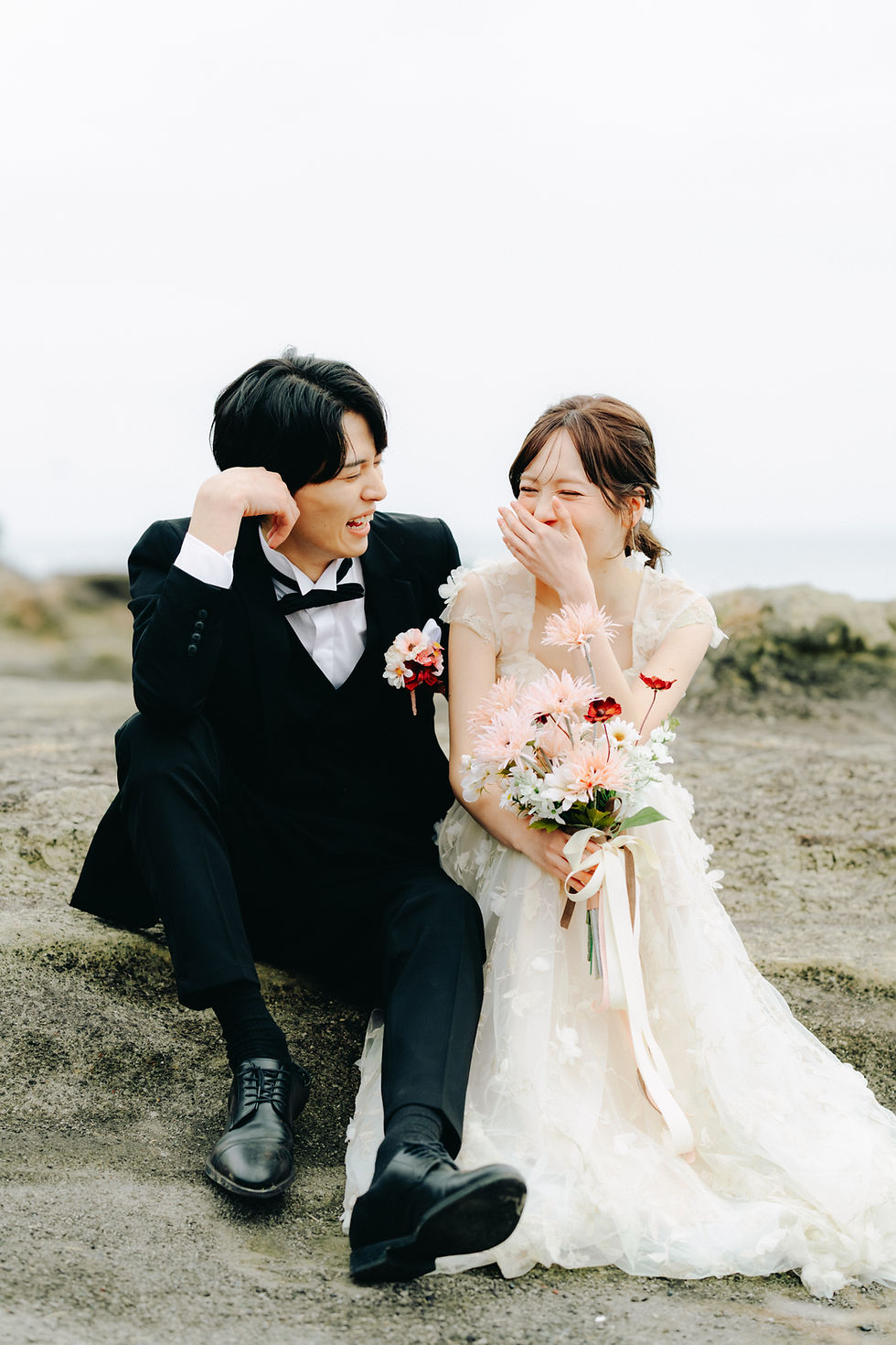城ヶ島の岩場で座って笑い合っている新郎新婦のウェディングフォト