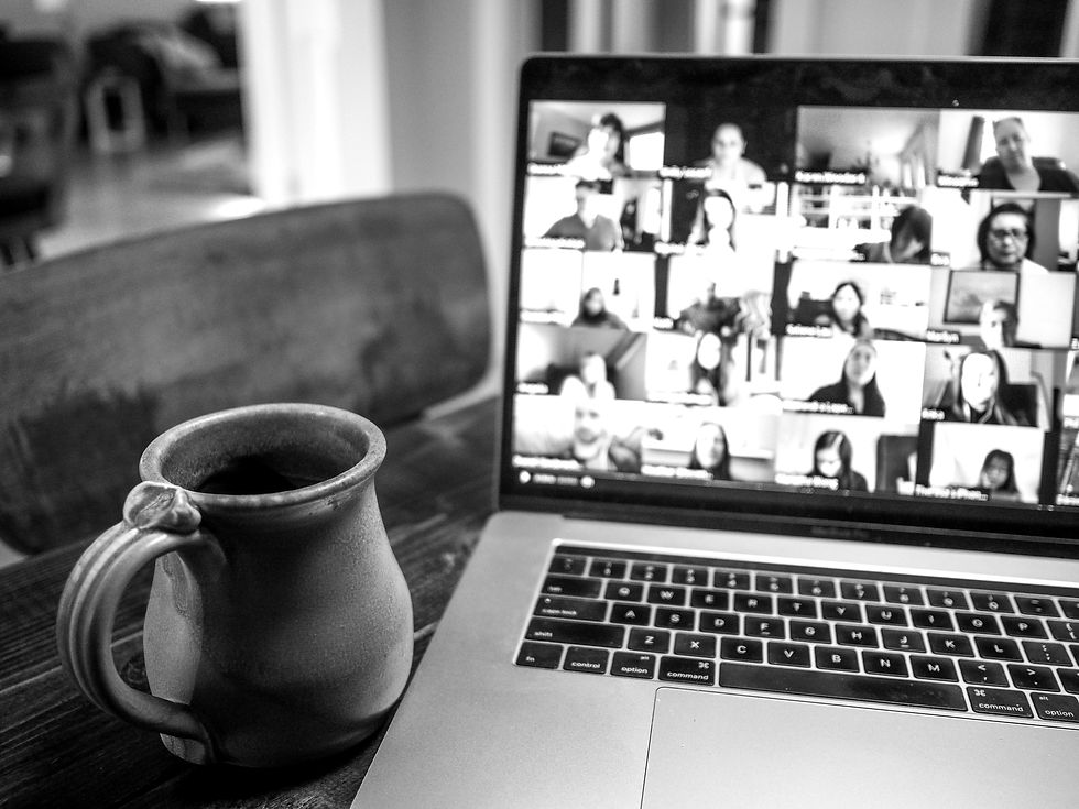An image of a laptop and coffee cup, with the user on a video with several other people