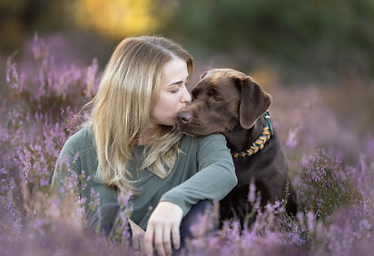 eine Frau küsst ihren Hund zwischen den Heideblüten der Lieberoser Heide