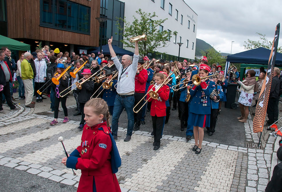 Marching band and majorettes parading through central Brattvåg, surrounded by a crowd of spectators