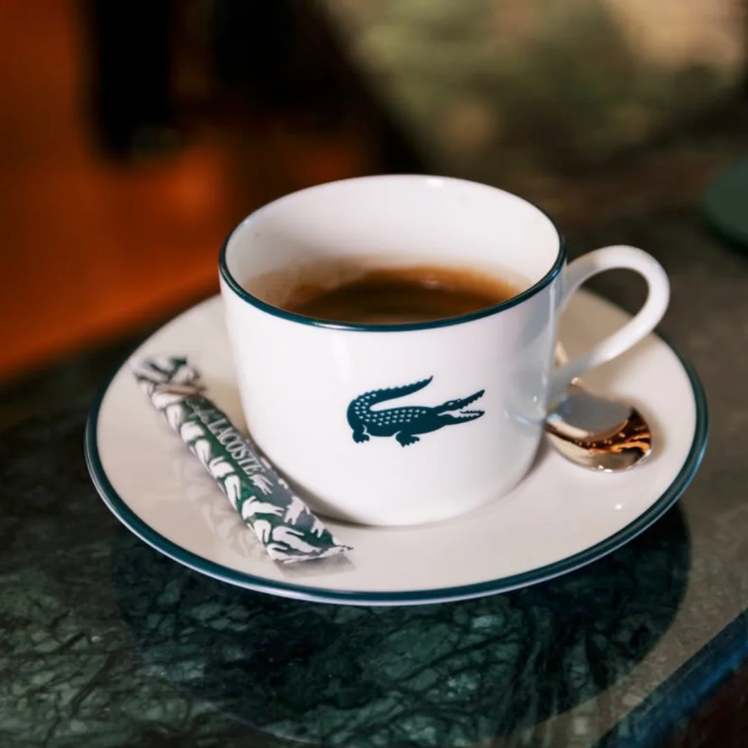 Xícara de café com o logotipo da Lacoste servida em pires branco no Café Lacoste em Paris.