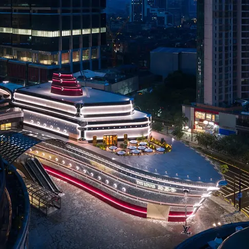 Fachada de “The Louis” à noite, com iluminação dourada destacando o formato de navio