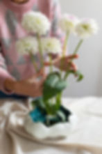 Pessoa montando arranjo floral minimalista com flores brancas e vaso orgânico — gesto simbólico inspirado na Ikebana como ritual de harmonia e contemplação.