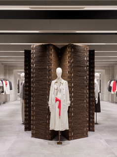 Interior da loja Zara com layout amplo e instalação central de exposição de roupas em espaço minimalista de concreto.