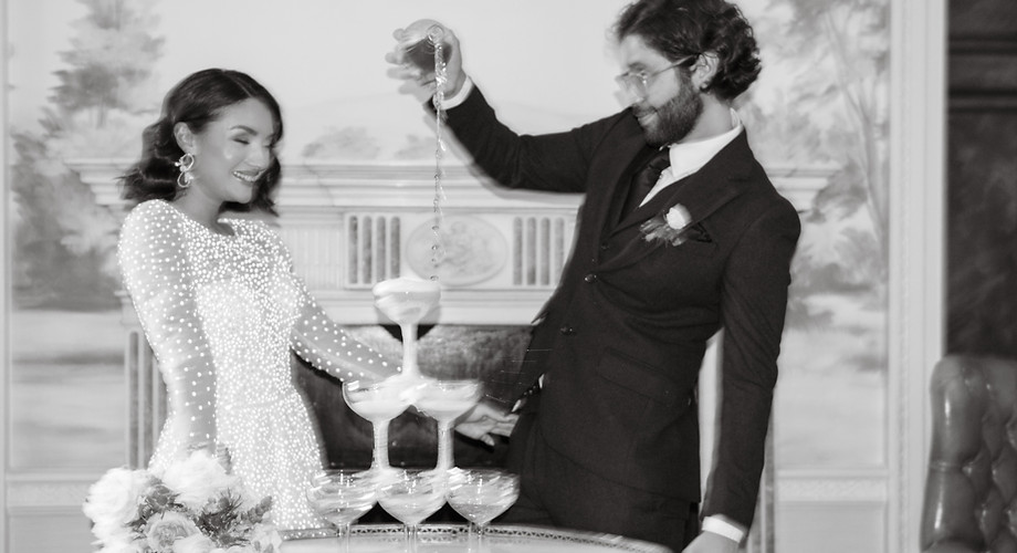 Bride and groom pouring champagne into a tower, sharing a joyful moment.