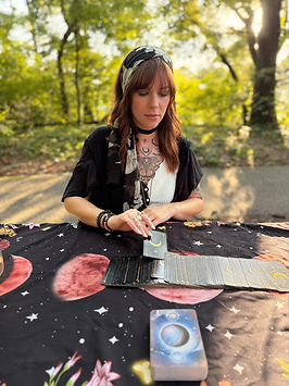 CA Rose, creative consultant, is seated at table outdoors, and pulls a tarot card to provide intuitive insight for a client.