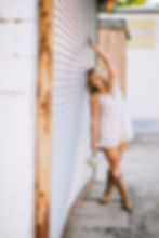 High school senior in a floral dress and cowboy boots posing beside a metal storefront
