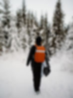 A person walking through a snowy forest wearing an orange jacket during a winter hike.