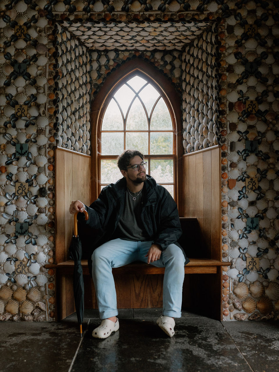 A man sitting inside a small arched alcove decorated with stacked logs.