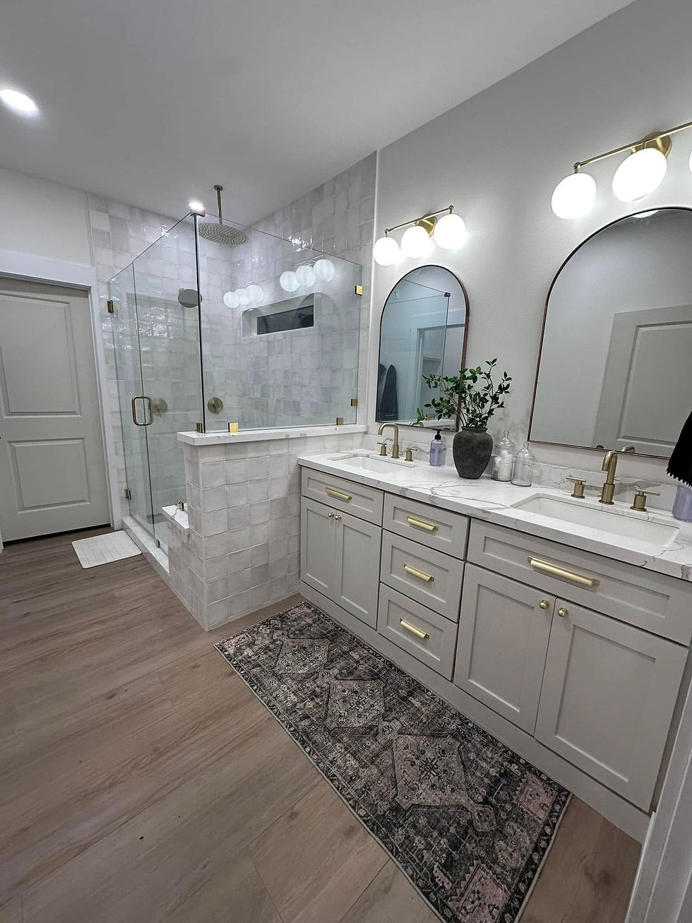 Remodeled bathroom with double vanity, arched mirrors and glass shower
