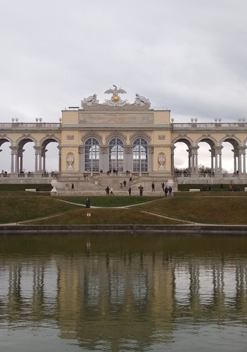 Gloriette Gebäude Schönbrunn, majestätisch reflektiert in ruhigem Wasser unter Wolken.