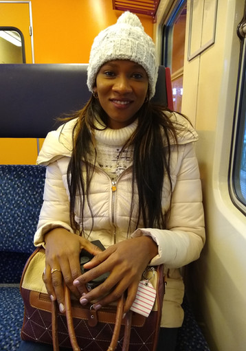 Schwarze Frau lächelt in weißer Winterkleidung sitzend in einem Zug.