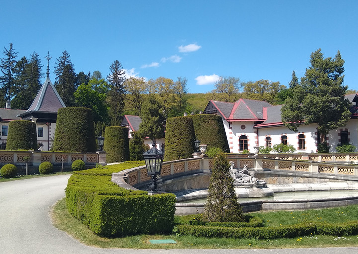 Herrschaftliches Anwesen mit formalen Gärten, Buchsbaumhecken und Springbrunnen. Blauer Himmel.