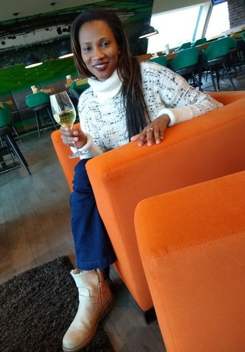 Frau sitzt lächelnd in orangefarbenem Sessel, hält Glas Weißwein.