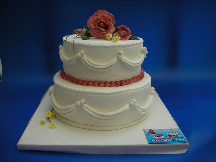 Two tier white wedding cake with fondant drapes and handmade peach sugar roses on top.