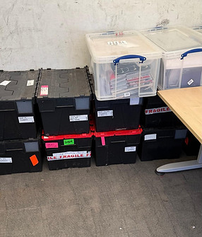 Stacks of heavy-duty black plastic commercial lidded crates with custom labels for finance logs and audit records sitting alongside clear plastic storage containers filled with corporate files and folders in a secure business archive facility.