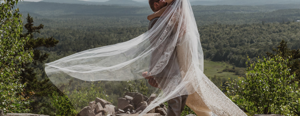Bride on groom on mountain top in Maine Wedding