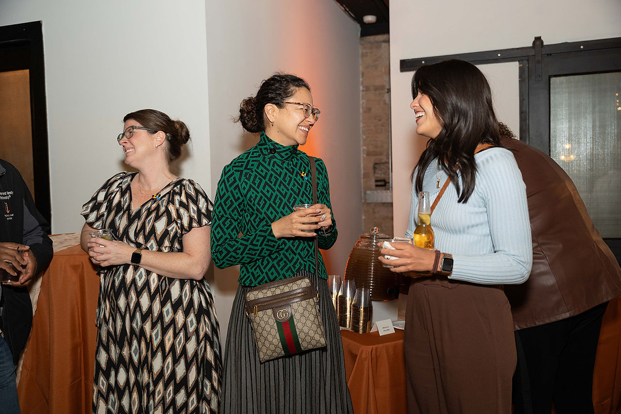 Three participants stand together holding drinks and talking during a social moment at the gathering.