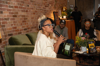 A speaker sits on a couch and gestures while speaking to an audience during a discussion.